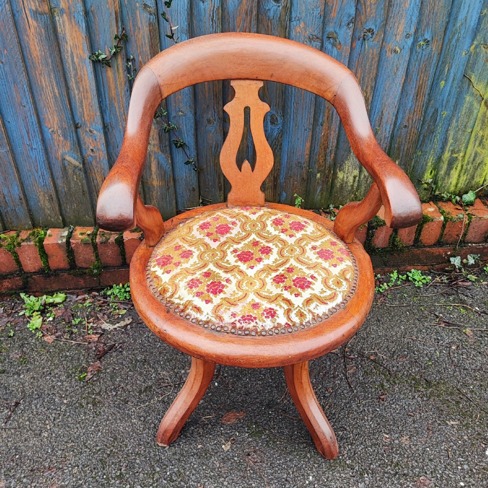A Victorian mahogany revolving desk chair featuring a curved horseshoe armrest, a pierced central back splat, and an upholstered circular seat.
