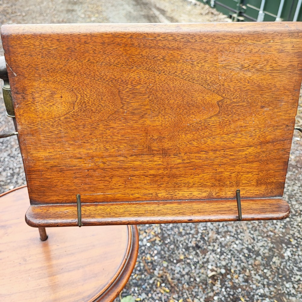 An antique Victorian adjustable mahogany reading stand featuring a revolving book rest with page holders, a secondary circular tray, and a telescopic brass stem on a cast iron base. View II