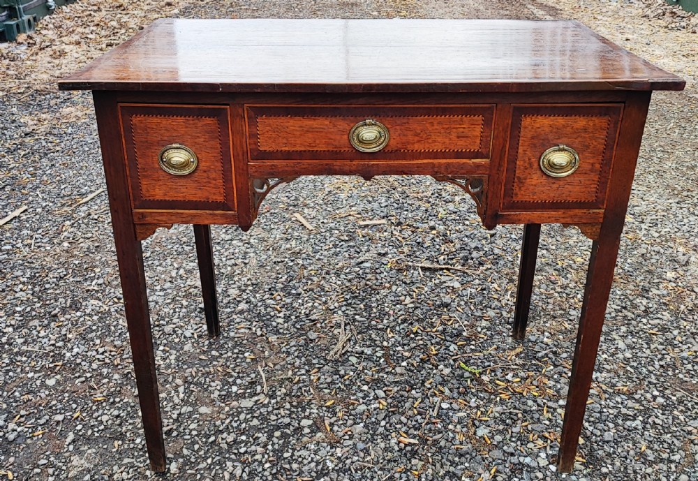 A Georgian dark oak lowboy side table featuring a rectangular top, three drawers with brass handles, inlaid stringing, corner spandrels, and straight tapering legs.