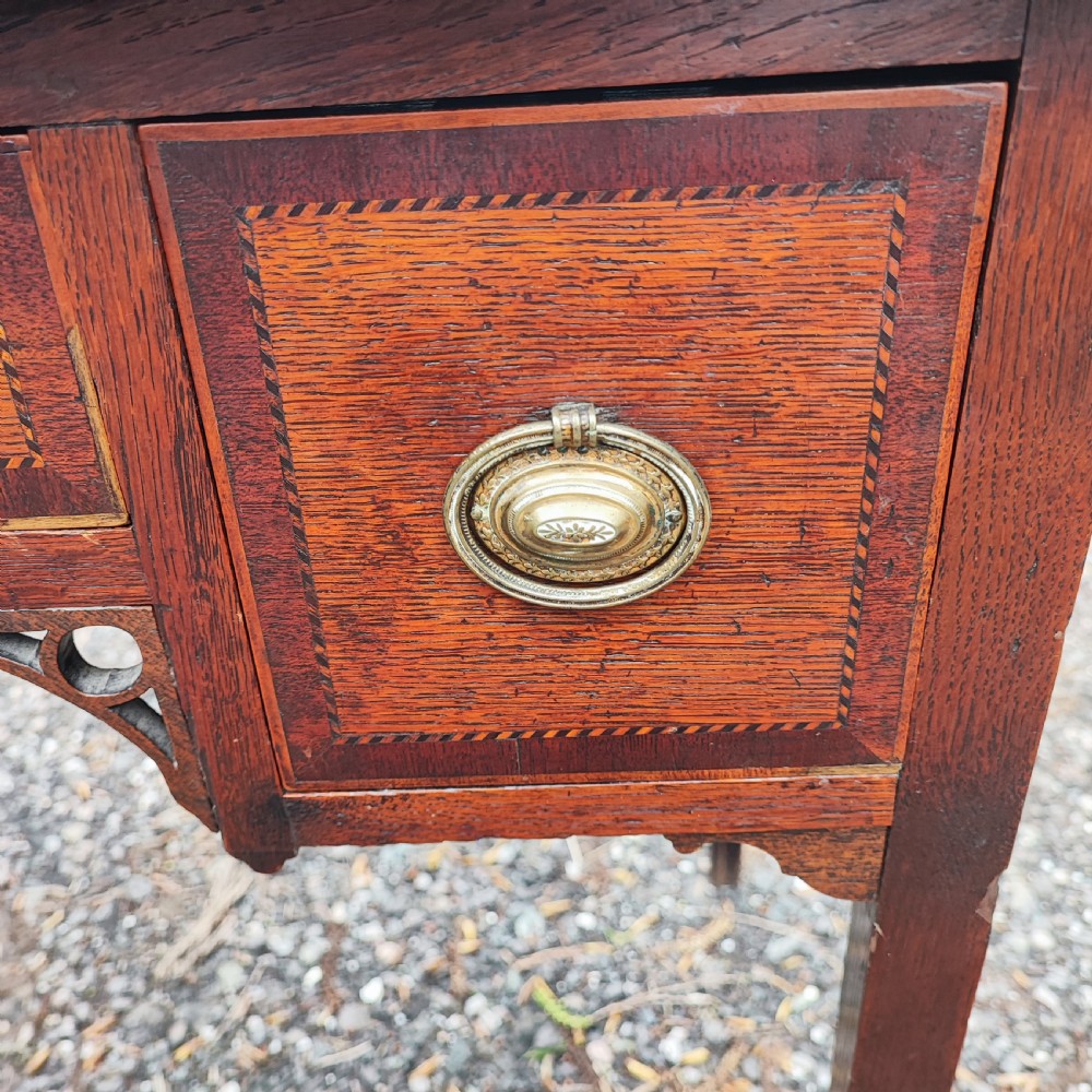 A Georgian dark oak lowboy side table featuring a rectangular top, three drawers with brass handles, inlaid stringing, corner spandrels, and straight tapering legs. View II