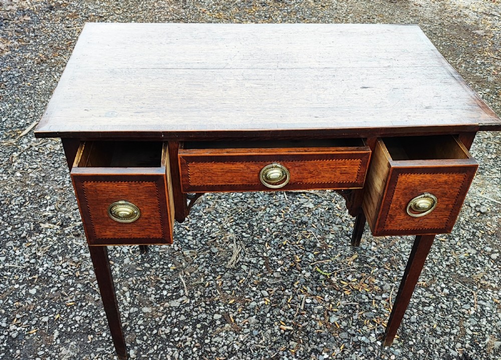 A Georgian dark oak lowboy side table featuring a rectangular top, three drawers with brass handles, inlaid stringing, corner spandrels, and straight tapering legs. View III