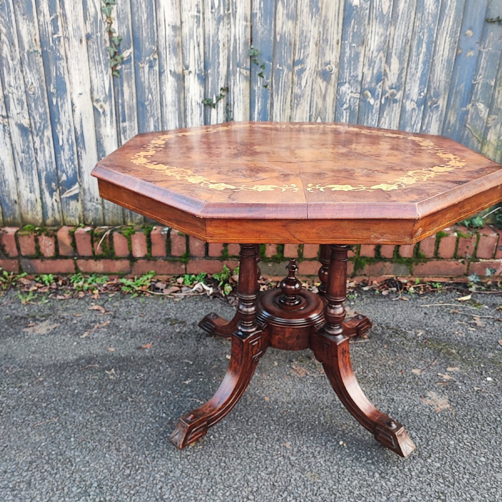 An octagonal Victorian centre table made of burr walnut featuring an inlaid floral marquetry border and a turned four-column pedestal base. View IV