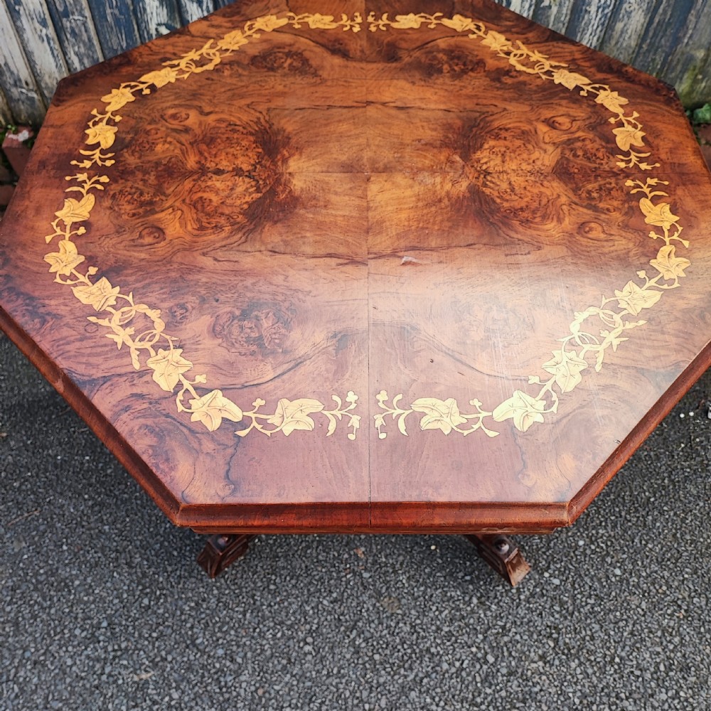 An octagonal Victorian centre table made of burr walnut featuring an inlaid floral marquetry border and a turned four-column pedestal base. View VI