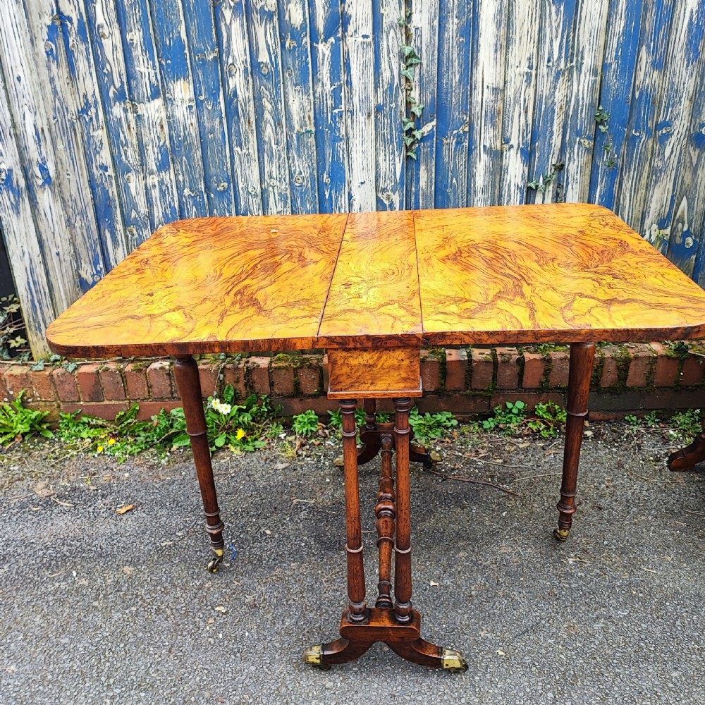 A Victorian burr walnut Sutherland table with extended drop leaves, turned twin-column supports, and brass castors.