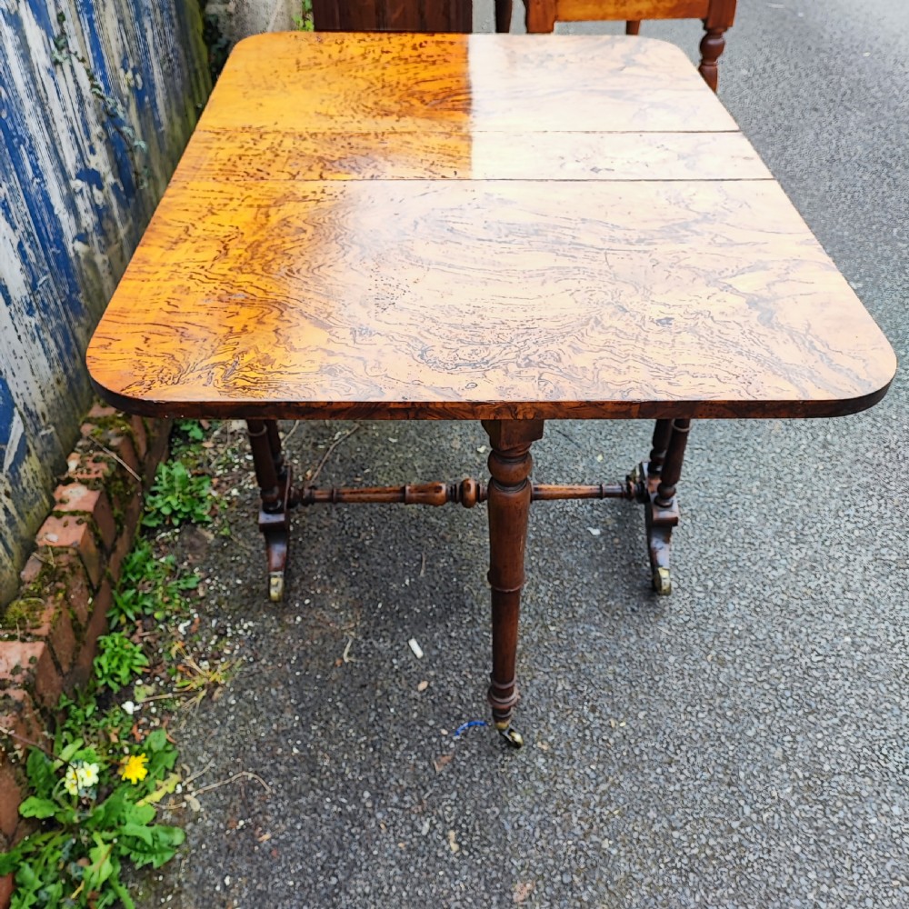 A Victorian burr walnut Sutherland table with extended drop leaves, turned twin-column supports, and brass castors. View II