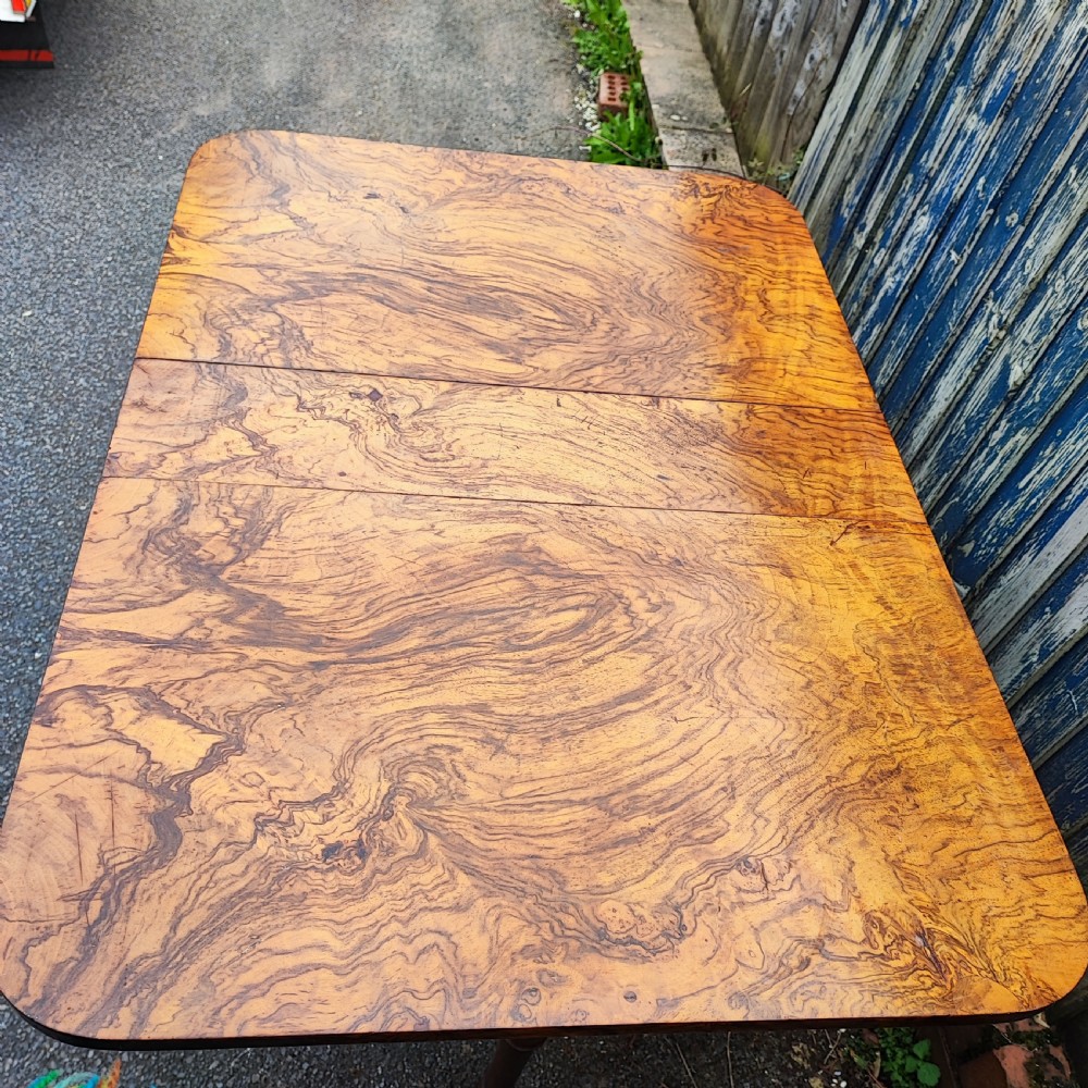 A Victorian burr walnut Sutherland table with extended drop leaves, turned twin-column supports, and brass castors. View III