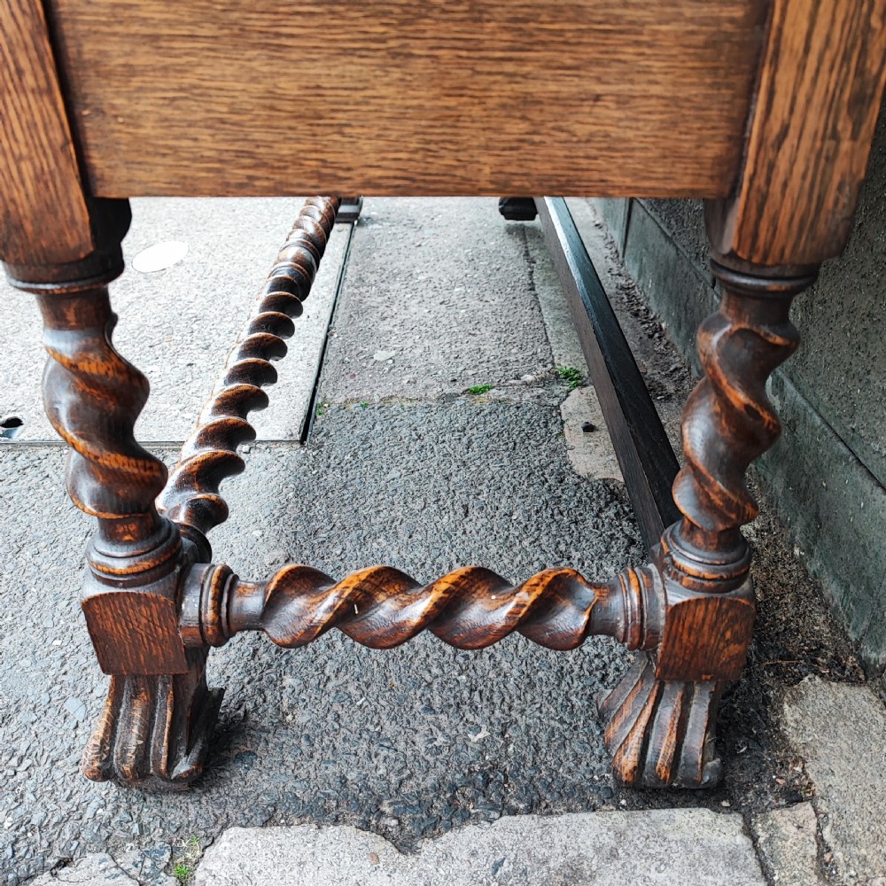 A warm brown oak Jacobean revival bookcase featuring double glazed doors with geometric diamond astragals, carved top frieze, and barley twist legs connected by a stretcher base. View IV