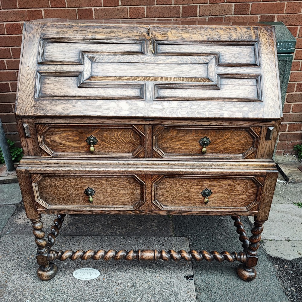 A Jacobean style oak bureau with geometric panelled drawers, a slant front writing lid, brass teardrop handles, and barley twist legs with a matching stretcher.