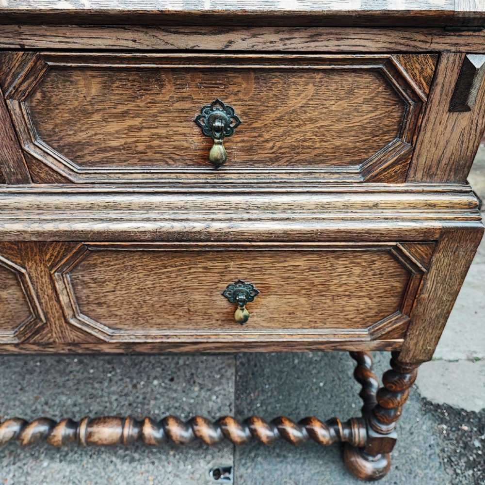 A Jacobean style oak bureau with geometric panelled drawers, a slant front writing lid, brass teardrop handles, and barley twist legs with a matching stretcher. View IV