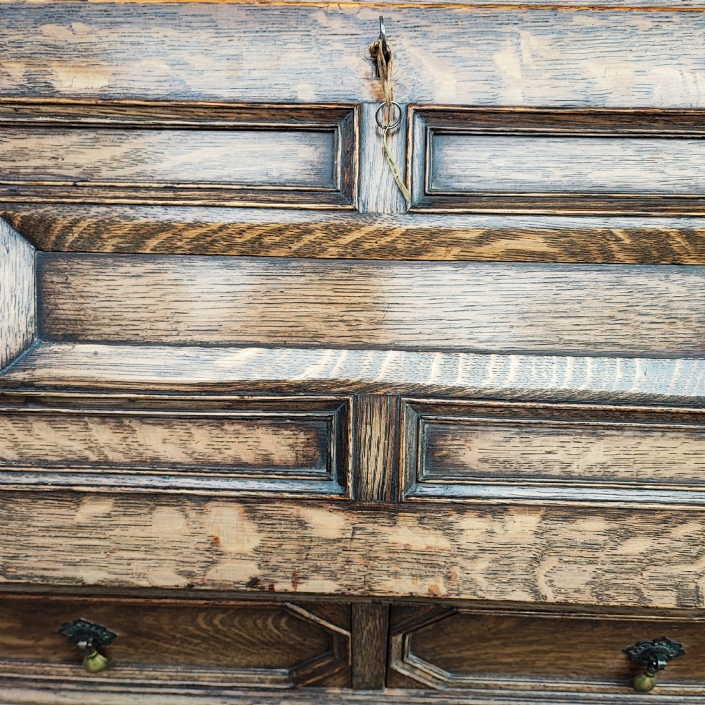 A Jacobean style oak bureau with geometric panelled drawers, a slant front writing lid, brass teardrop handles, and barley twist legs with a matching stretcher. View V