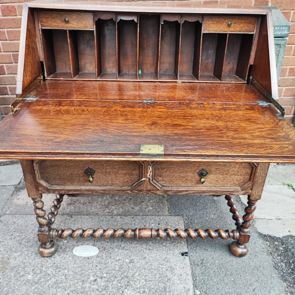 A Jacobean style oak bureau with geometric panelled drawers, a slant front writing lid, brass teardrop handles, and barley twist legs with a matching stretcher. View VIII