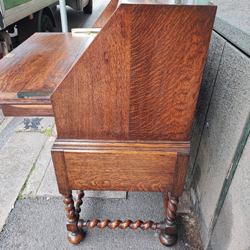 A Jacobean style oak bureau with geometric panelled drawers, a slant front writing lid, brass teardrop handles, and barley twist legs with a matching stretcher. View IX
