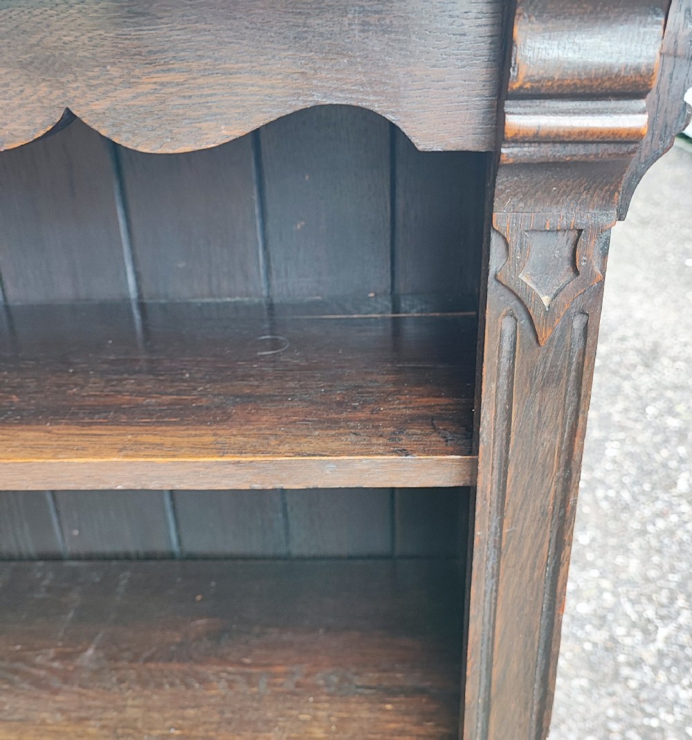 A dark oak open bookcase featuring five horizontal shelves, a scalloped upper frieze, vertical panelled backboards, and rounded bun feet. View V