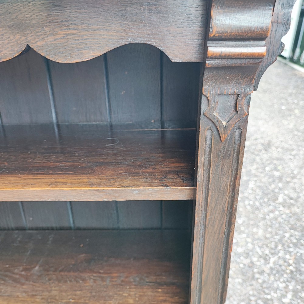 A dark oak open bookcase featuring five horizontal shelves, a scalloped upper frieze, vertical panelled backboards, and rounded bun feet. View VII