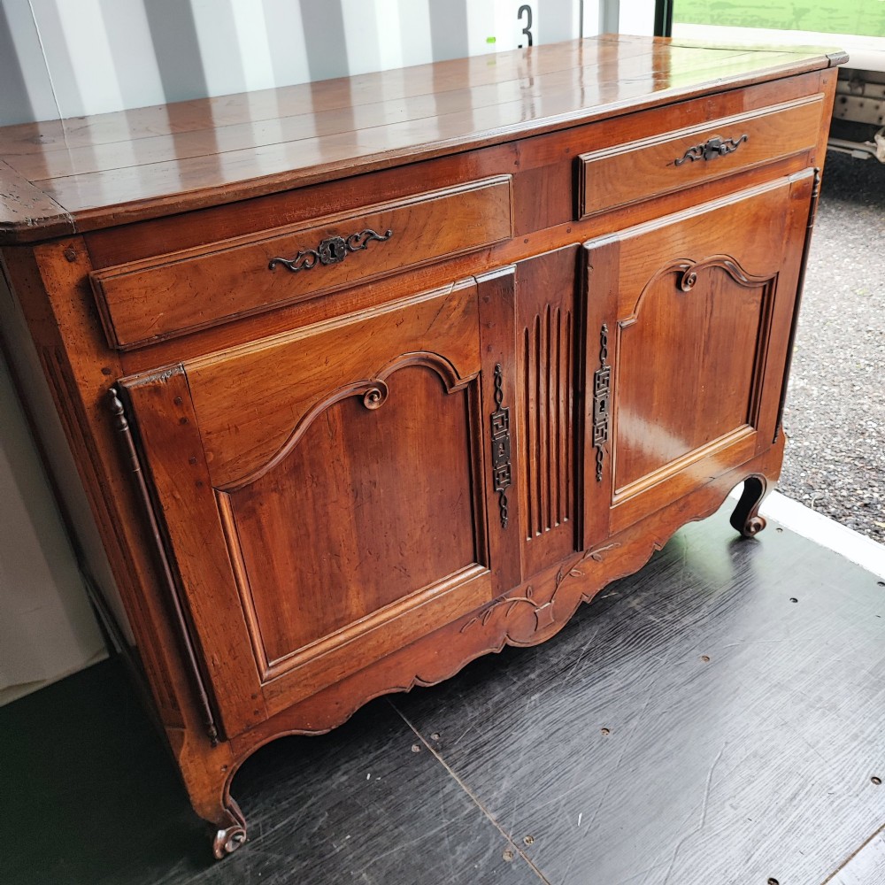 An 18th century French cherry wood side cabinet featuring two drawers above two carved panel doors with ornate metal escutcheons and cabriole feet.