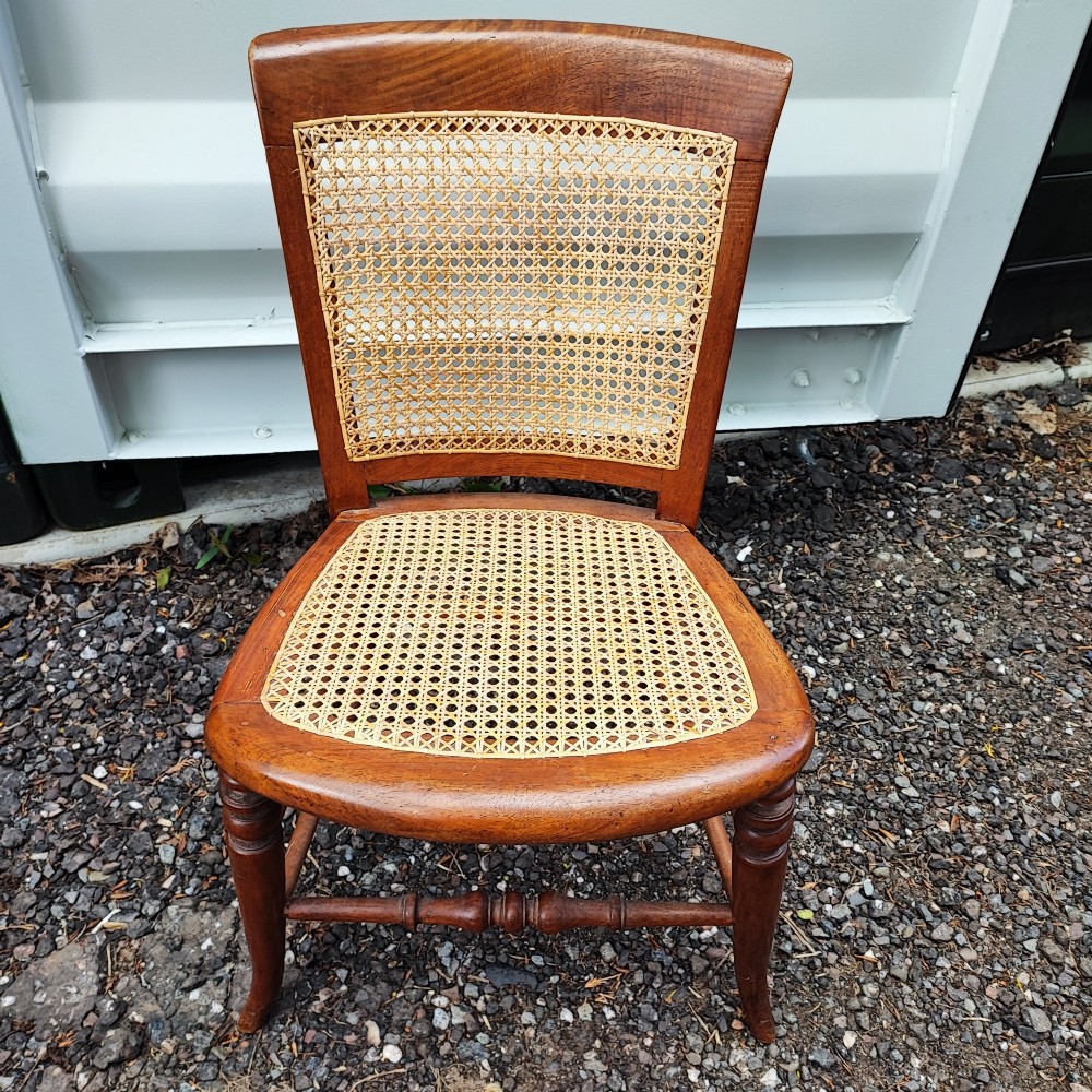 An antique mahogany chair featuring a curved backrest, turned front legs, and woven cane panels set into the seat and back. View V