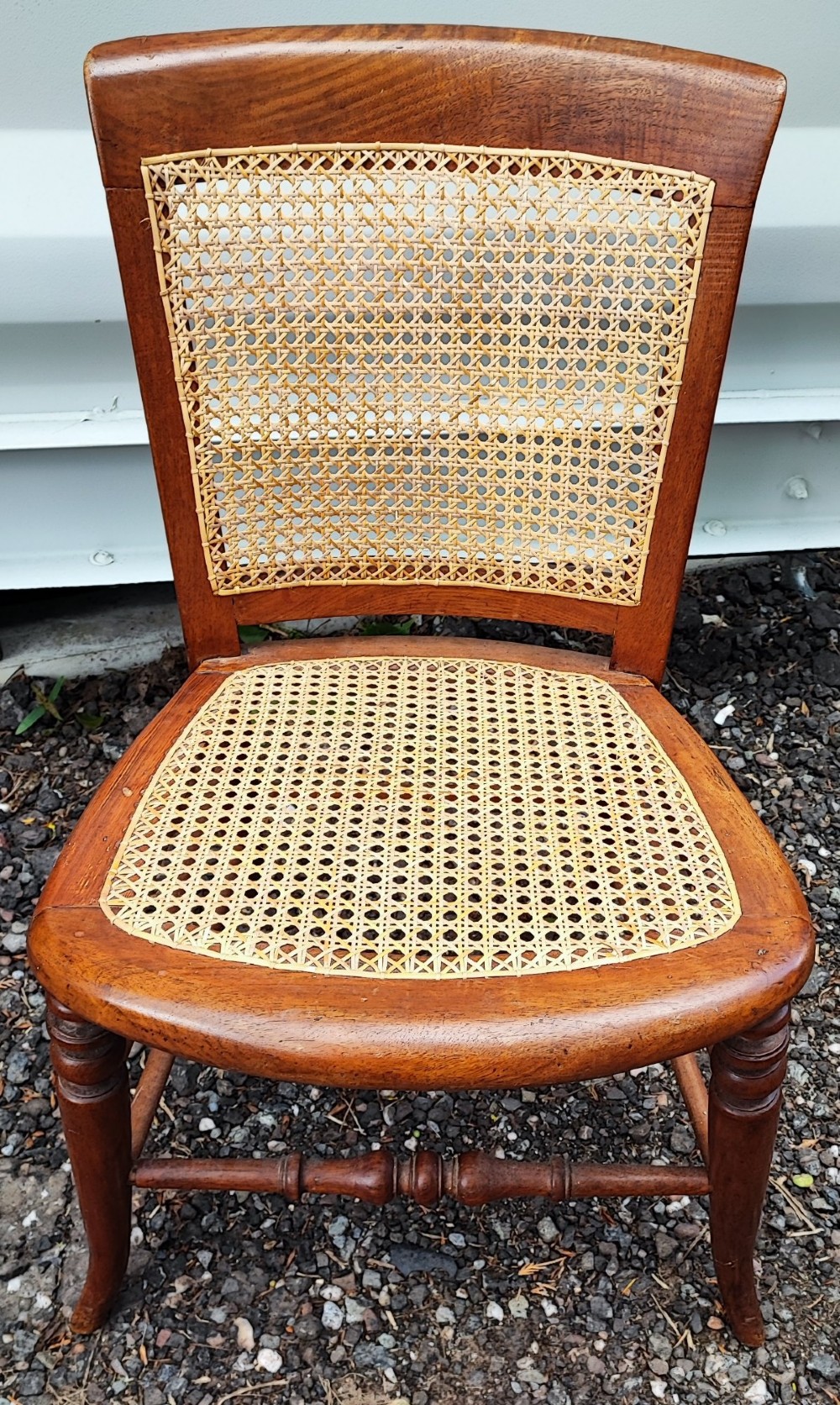 An antique mahogany chair featuring a curved backrest, turned front legs, and woven cane panels set into the seat and back. View VI