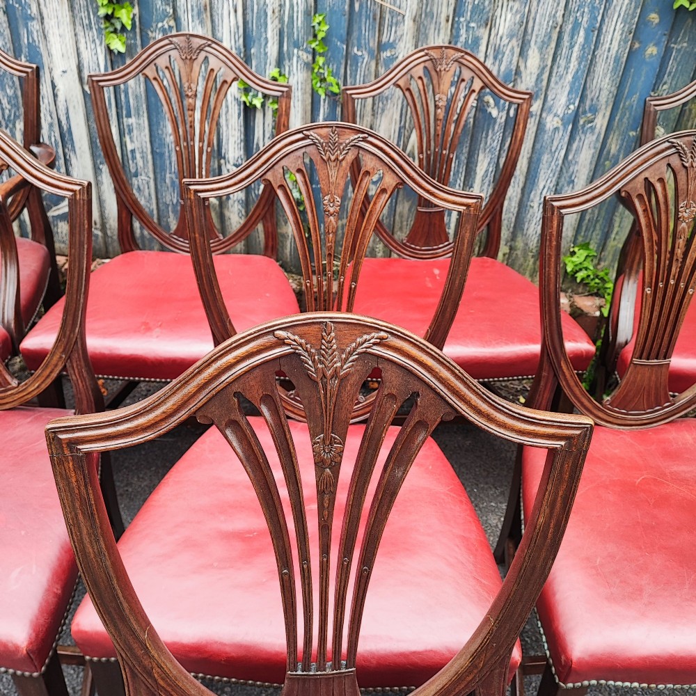 A set of eight mahogany Georgian-style dining chairs featuring carved wheat sheaf shield backs and red leather seats. View VI