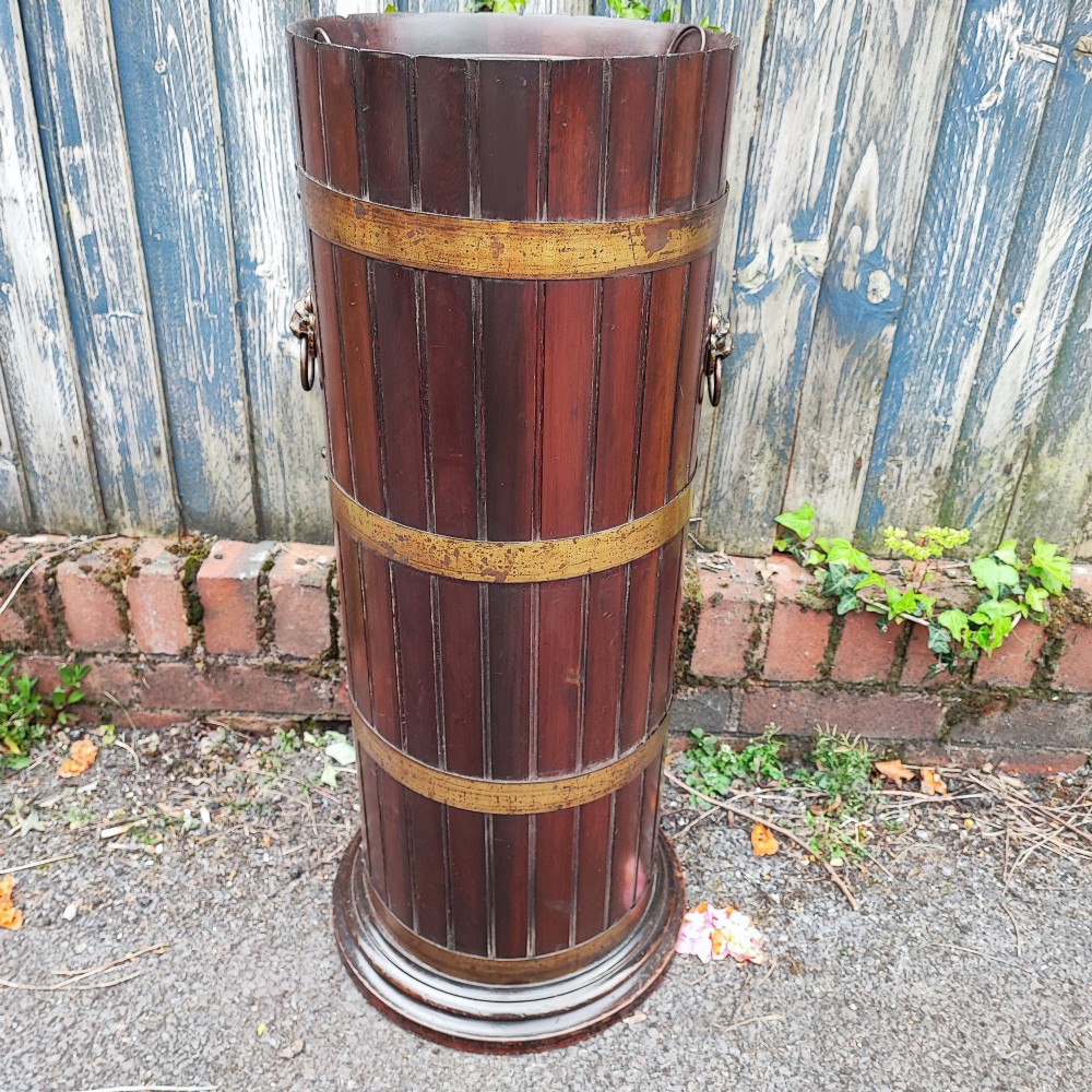 A cylindrical dark mahogany umbrella stand featuring three brass binding hoops, side ring handles, and a moulded circular base.