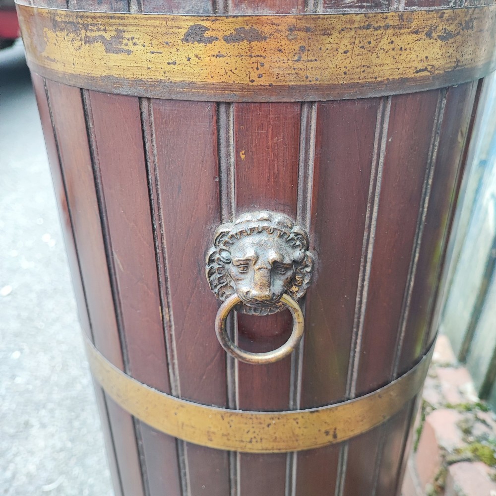 A cylindrical dark mahogany umbrella stand featuring three brass binding hoops, side ring handles, and a moulded circular base. View II