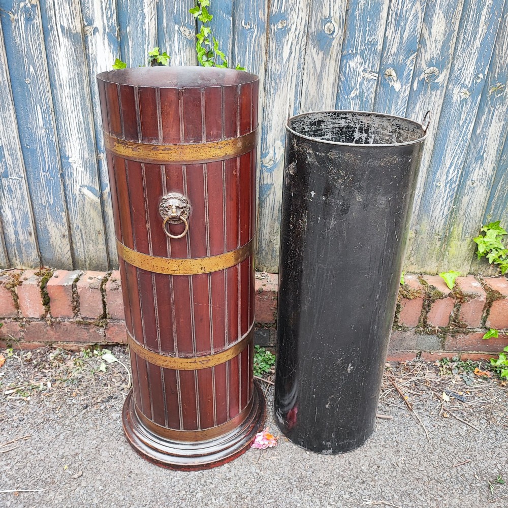 A cylindrical dark mahogany umbrella stand featuring three brass binding hoops, side ring handles, and a moulded circular base. View IV