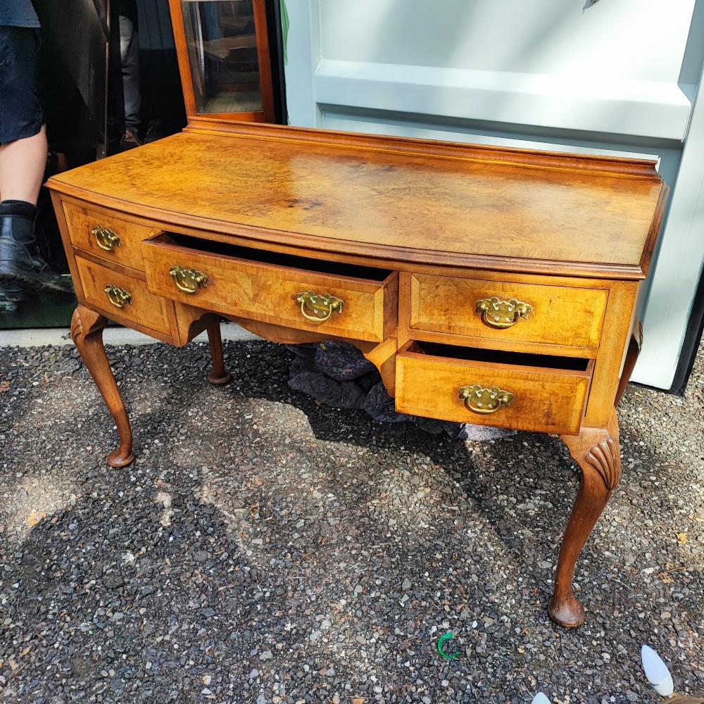 An antique burr walnut writing table featuring five drawers, brass handles, and carved cabriole legs.