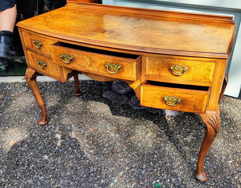 An antique burr walnut writing table featuring five drawers, brass handles, and carved cabriole legs. View IV