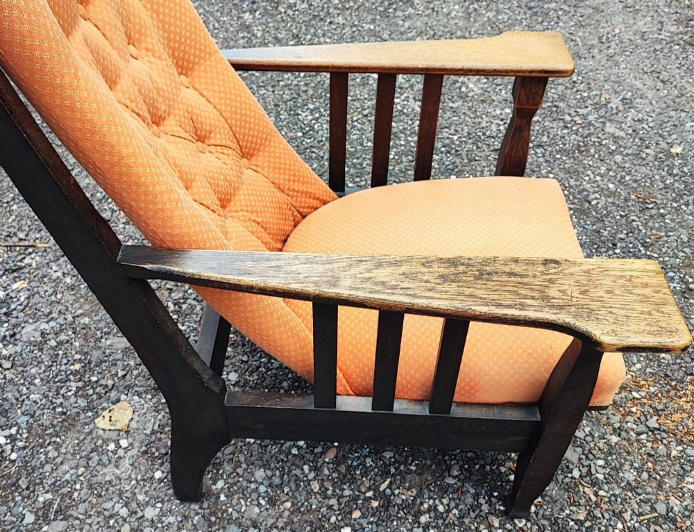 An antique Arts and Crafts oak reclining armchair with broad flat armrests, slatted sides, and orange buttoned upholstery. View II