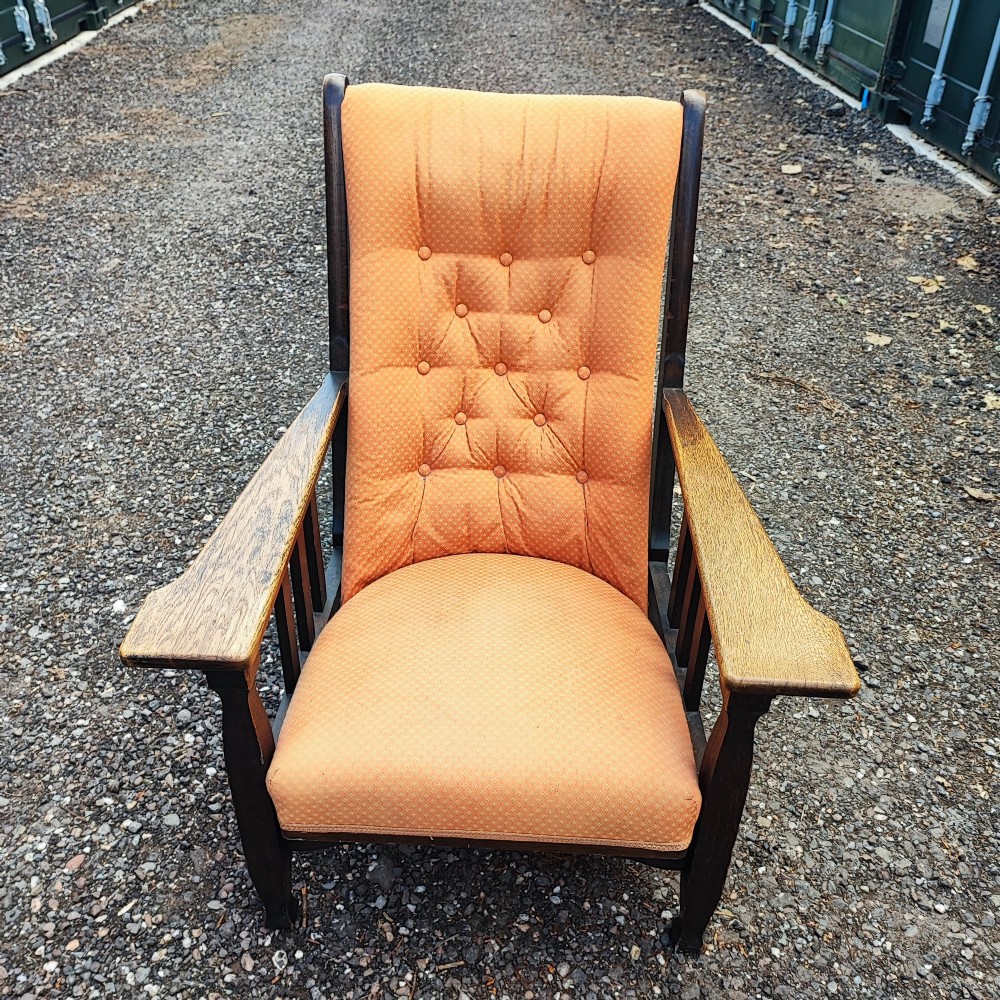 An antique Arts and Crafts oak reclining armchair with broad flat armrests, slatted sides, and orange buttoned upholstery. View V