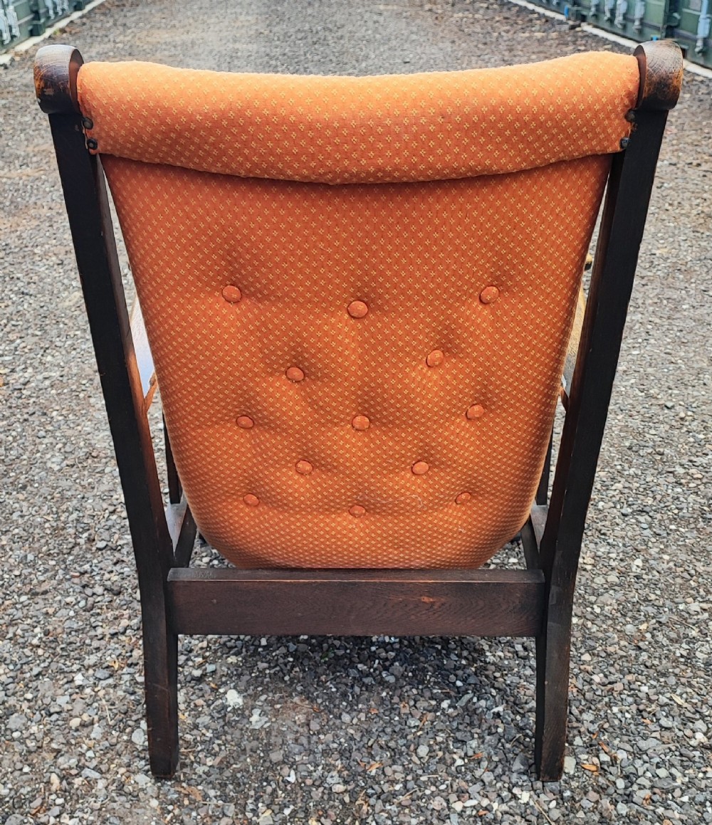 An antique Arts and Crafts oak reclining armchair with broad flat armrests, slatted sides, and orange buttoned upholstery. View VI