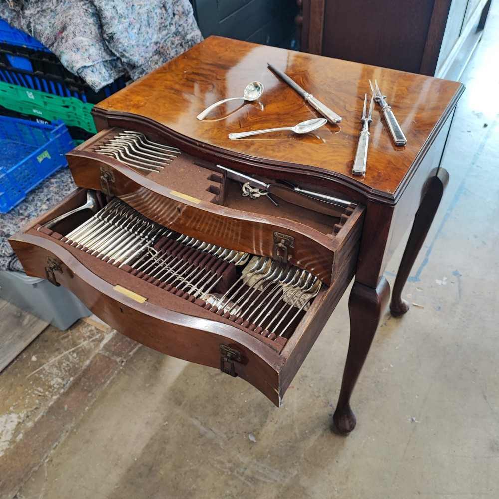 An open burr walnut cutlery canteen table featuring two fitted drawers containing rows of silver-plated flatware.