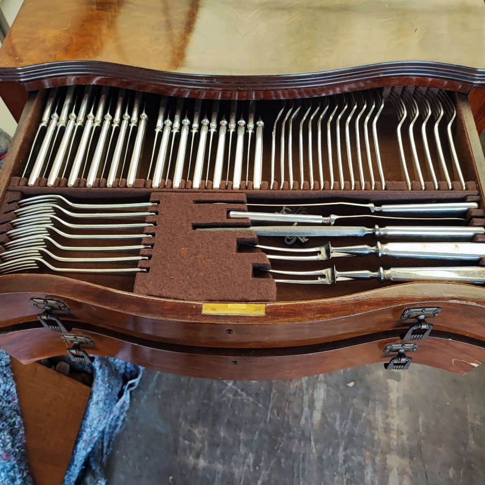 An open burr walnut cutlery canteen table featuring two fitted drawers containing rows of silver-plated flatware. View IV