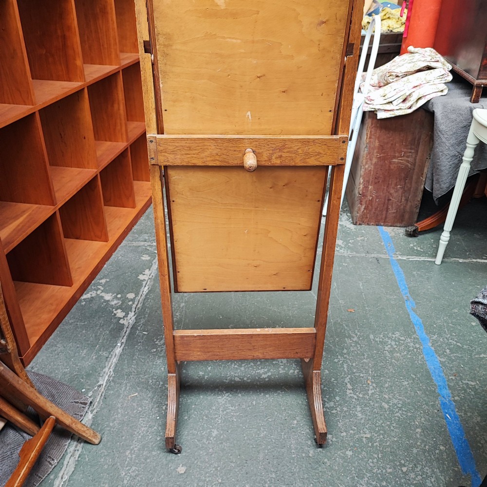 An Arts and Crafts oak cheval mirror featuring a tall bevelled glass plate supported between two square upright posts on splayed legs with castors. View III