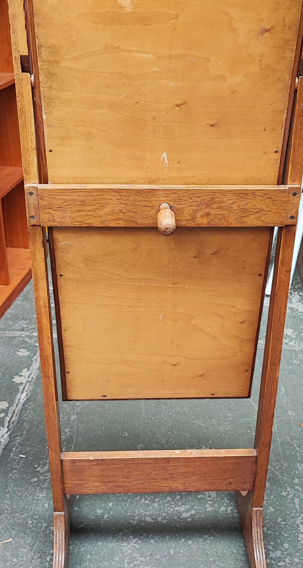 An Arts and Crafts oak cheval mirror featuring a tall bevelled glass plate supported between two square upright posts on splayed legs with castors. View VI