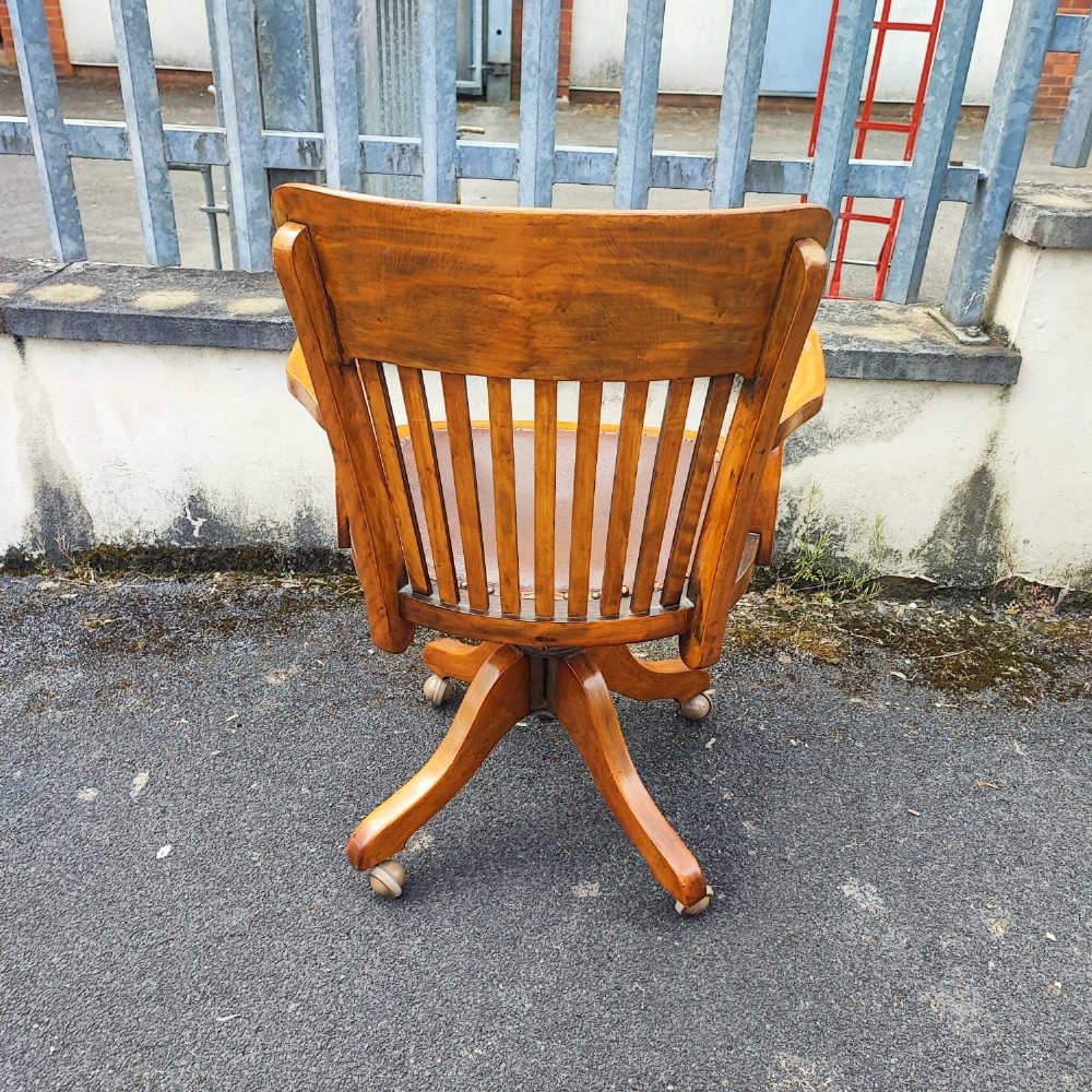 An antique mahogany revolving desk chair featuring a curved slatted back, studded leather seat, and a quadruped swivel base on castors. View II