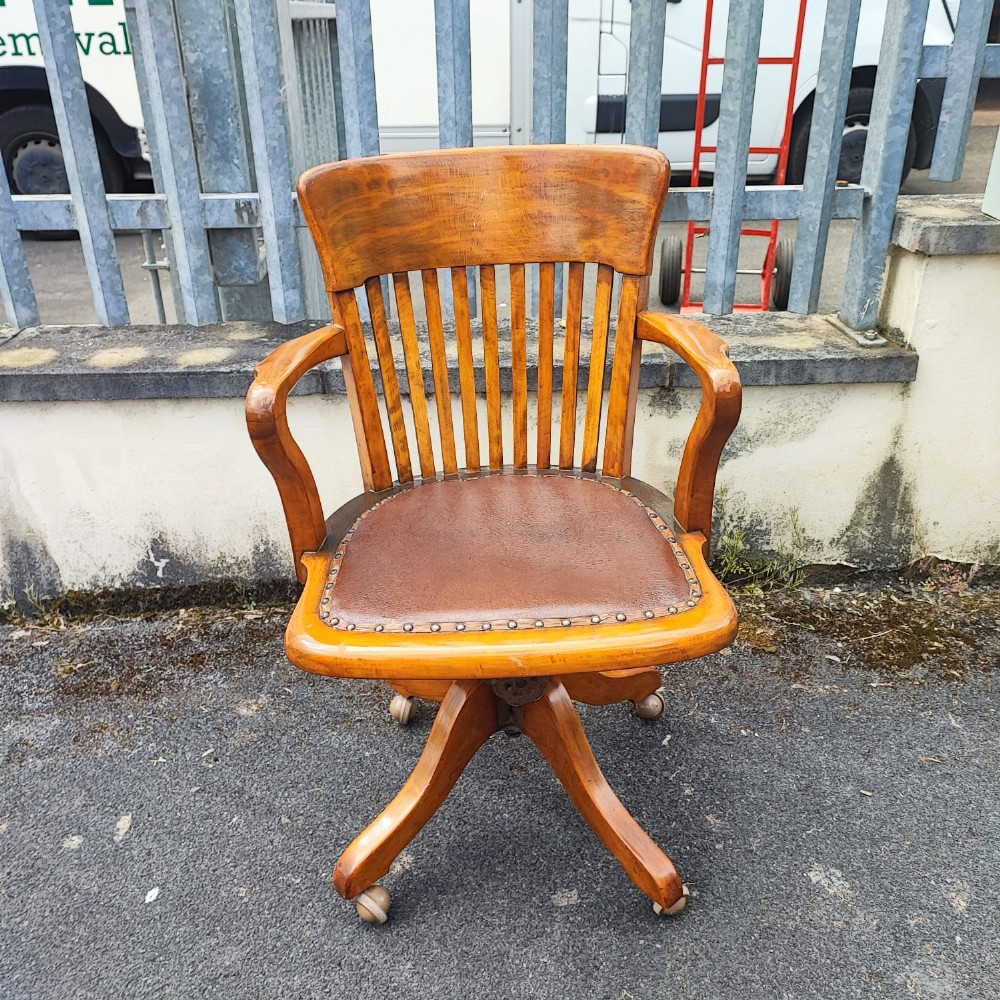 An antique mahogany revolving desk chair featuring a curved slatted back, studded leather seat, and a quadruped swivel base on castors. View III