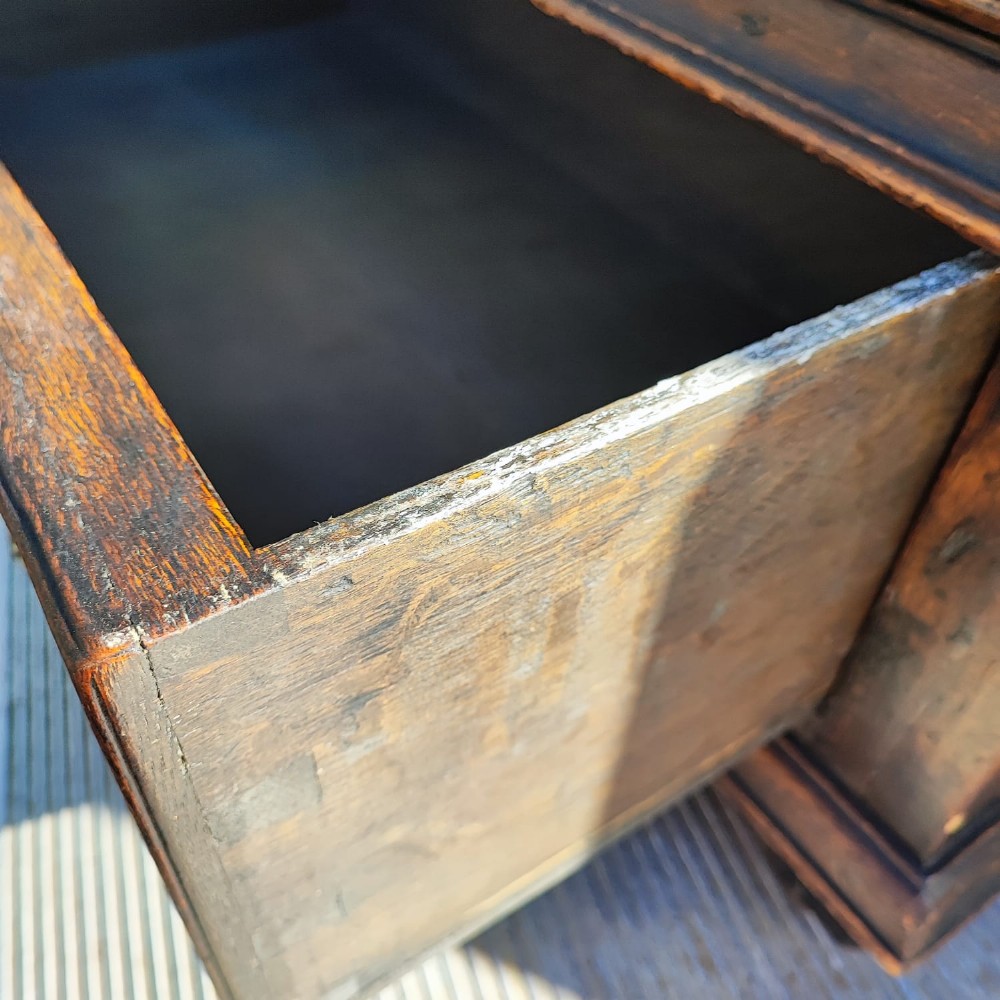 A dark oak Jacobean chest of drawers featuring geometric panel moulding, a carved top drawer, and brass drop handles. View III
