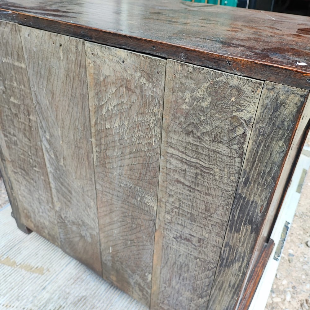 A dark oak Jacobean chest of drawers featuring geometric panel moulding, a carved top drawer, and brass drop handles. View IV