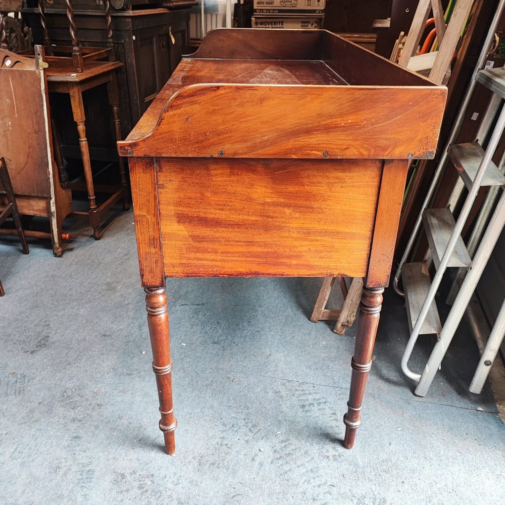 A Regency mahogany writing table featuring five drawers with circular brass backplates, a gallery back, an arched kneehole, and ring-turned legs. View III