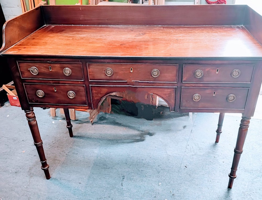 A Regency mahogany writing table featuring five drawers with circular brass backplates, a gallery back, an arched kneehole, and ring-turned legs. View V