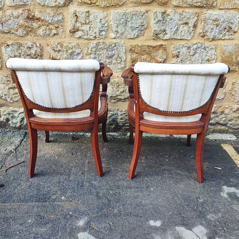 A matching pair of French antique armchairs crafted from polished brown wood with curved arms, cabriole legs, and cream striped fabric upholstery with studded borders. View II
