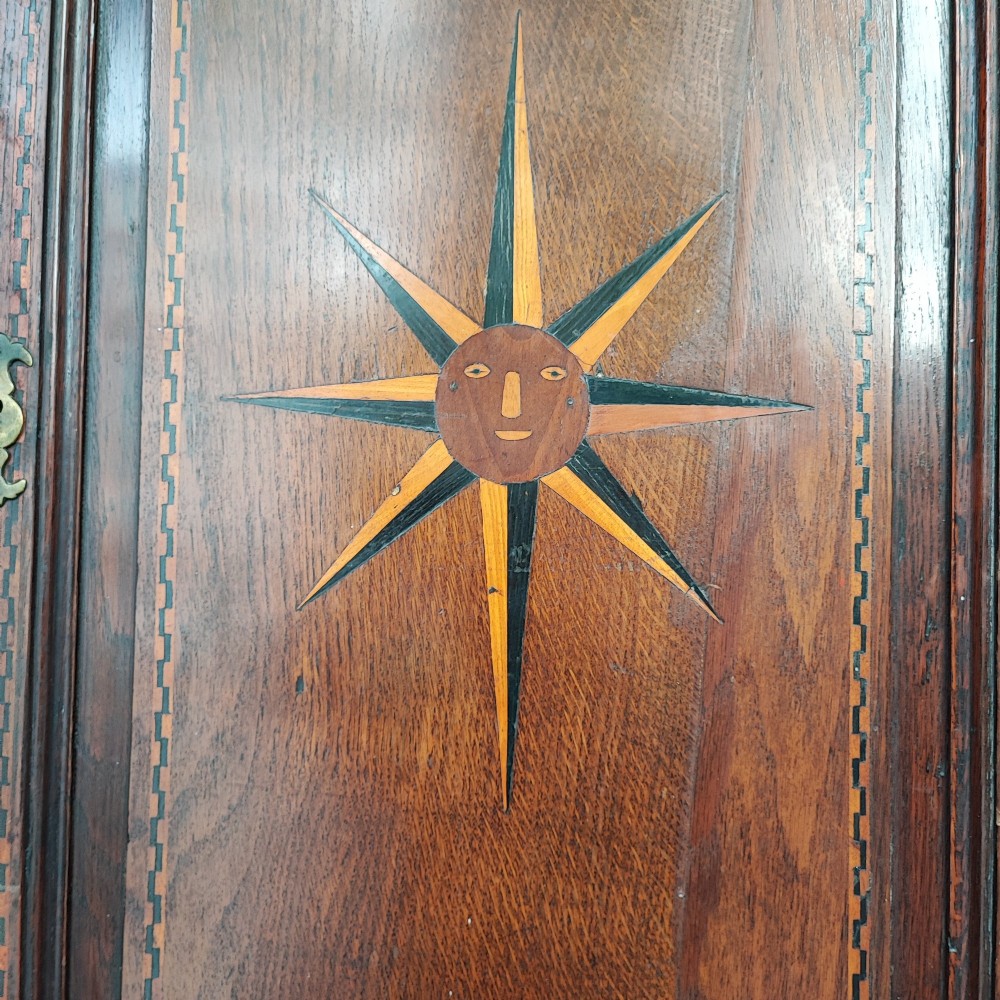 An antique brown oak hanging corner cupboard featuring a central sunburst inlaid door panel, chequered border stringing, and decorative brass hinges. View II