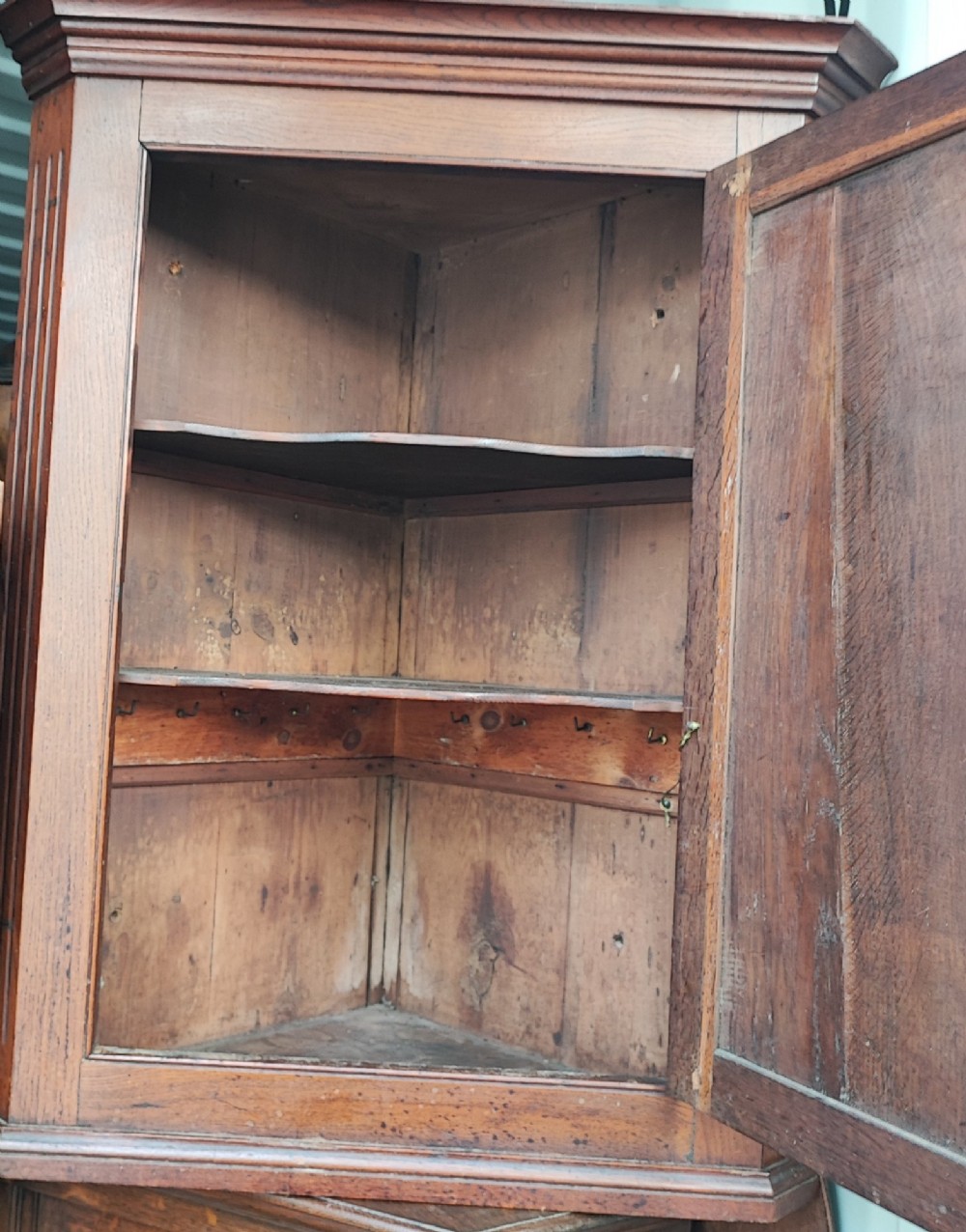 An antique brown oak hanging corner cupboard featuring a central sunburst inlaid door panel, chequered border stringing, and decorative brass hinges. View VI