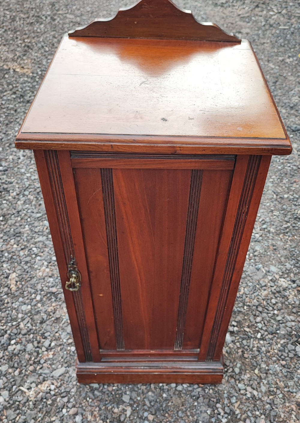 An Edwardian mahogany bedside cabinet with a shaped splashback, reeded door moulding, and a single brass drop handle. View II