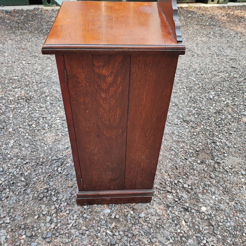 An Edwardian mahogany bedside cabinet with a shaped splashback, reeded door moulding, and a single brass drop handle. View VII