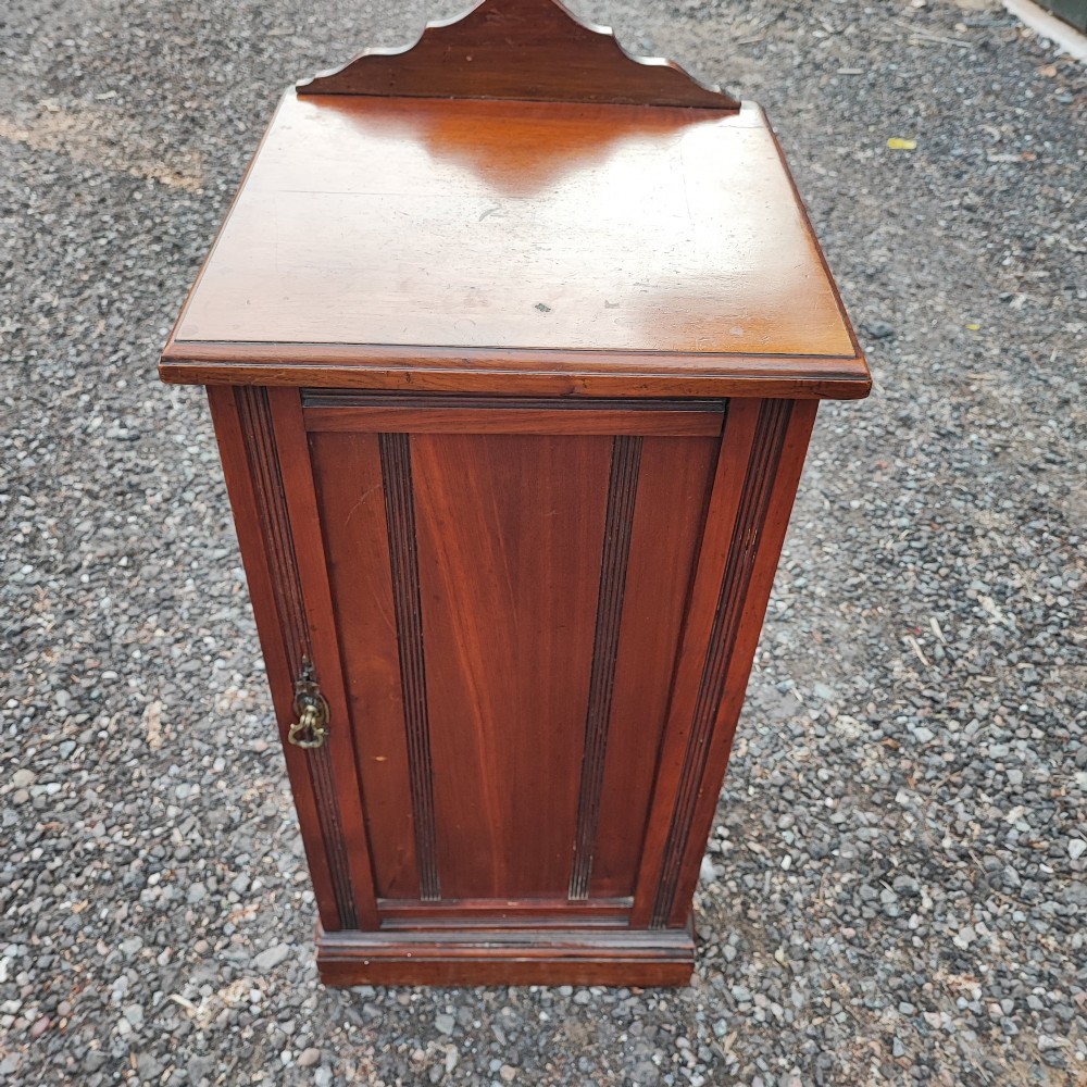 An Edwardian mahogany bedside cabinet with a shaped splashback, reeded door moulding, and a single brass drop handle. View VIII