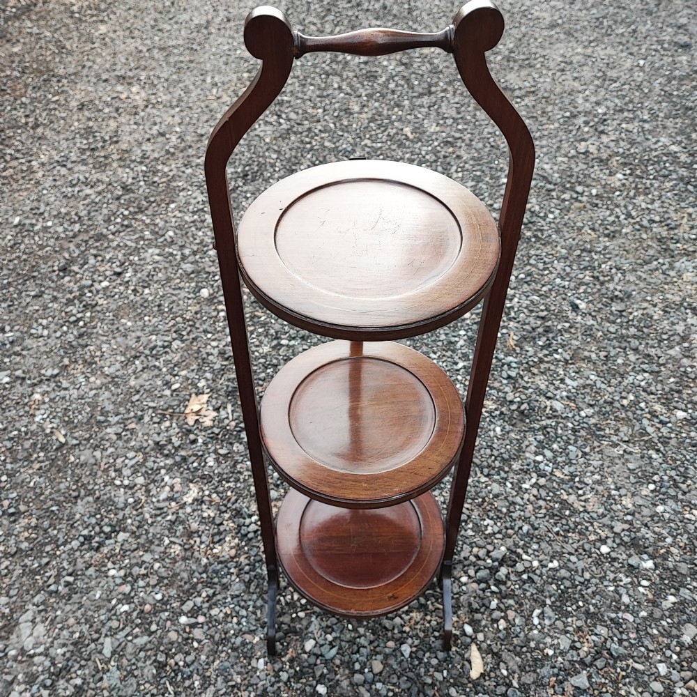 An Edwardian three-tier mahogany cake stand with boxwood string inlay, circular trays, and a arched top carrying handle. View VI