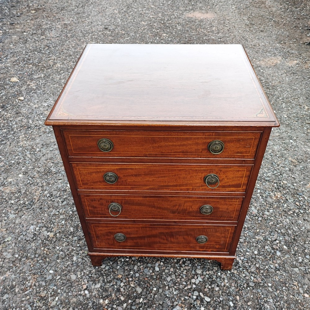 An Edwardian mahogany chest of four drawers featuring boxwood stringing inlay, crossbanded top, circular brass ring handles, and bracket feet.