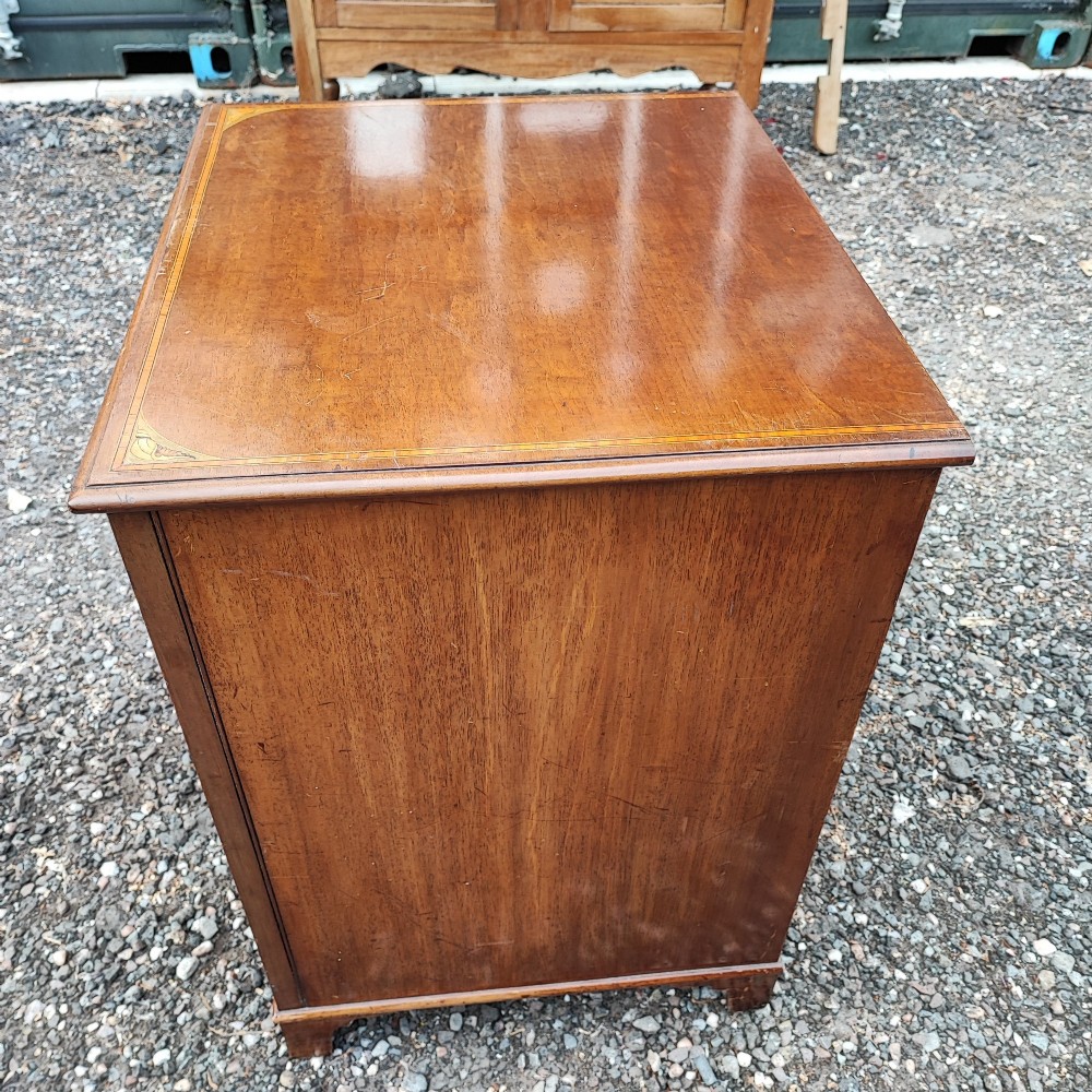 An Edwardian mahogany chest of four drawers featuring boxwood stringing inlay, crossbanded top, circular brass ring handles, and bracket feet. View IV