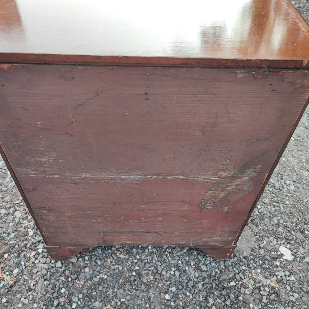 An Edwardian mahogany chest of four drawers featuring boxwood stringing inlay, crossbanded top, circular brass ring handles, and bracket feet. View V